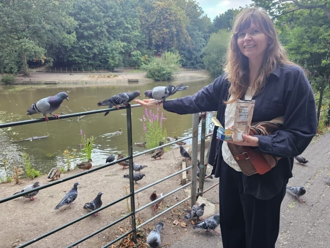 Jessica Friday feeding a crowd of pigeons from her hand beside a pond